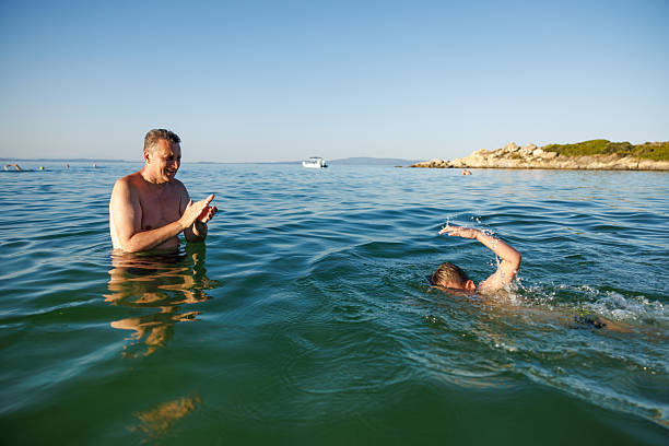 Father gently supporting his son in shallow sea water, teaching him how to swim