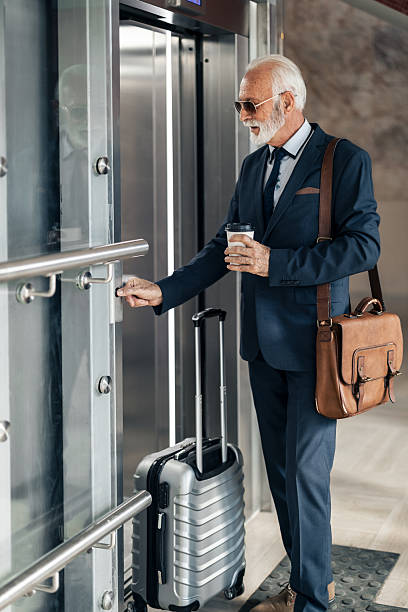 istock Senior Businessman Entering Elevator With Luggage and Coffee Cup 2214210601