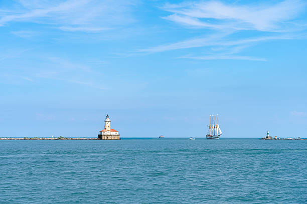 Four-masted sailing ship navigating on lake michigan with chicago harbor lighthouse in the background, on a sunny day with blue sky and calm sea