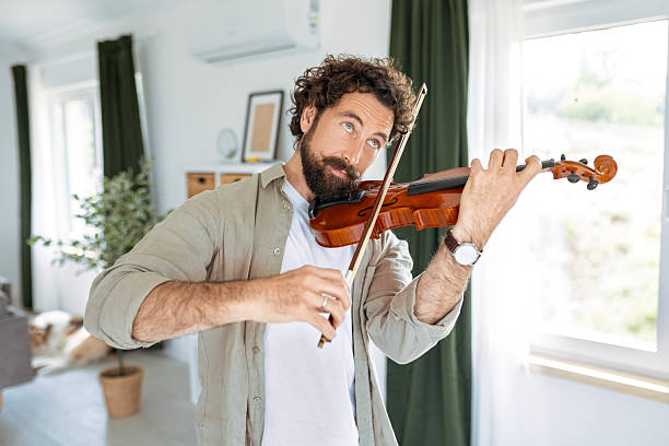 istock Man Playing Violin in Sunlit Living Room 2214214770