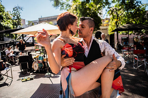 Couple dancing tango in a public square. There is live music equipment in the background and people watching under umbrellas, enjoying the sunny day in Buenos Aires, Argentina