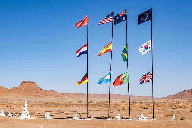 Colorful flags representing various nations waving in a desert landscape, showcasing cultural diversity amid the vastness of Morocco's Sahara during the spring season.