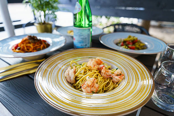 An outdoor table set with colorful Italian pasta dishes and a bottle of sparkling water, creating a fresh and inviting Mediterranean dining atmosphere.