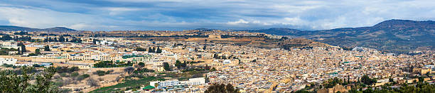 Panoramic view of Fes, a historic city in Morocco, showcasing a dense urban landscape with surrounding natural scenery under a picturesque blue sky.