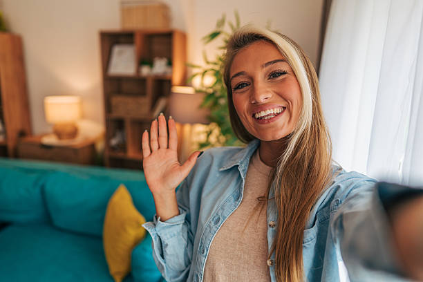 istock Young woman waving hand while taking selfie at home 2214232268