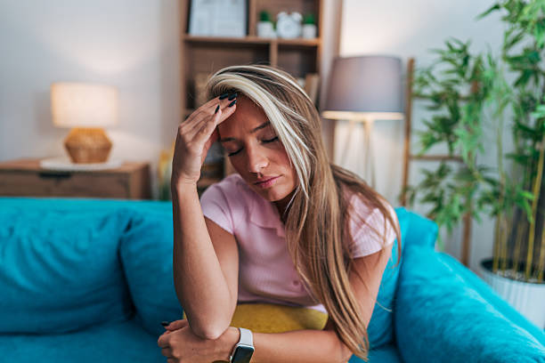 istock Young woman suffering from headache while sitting on sofa at home 2214239835
