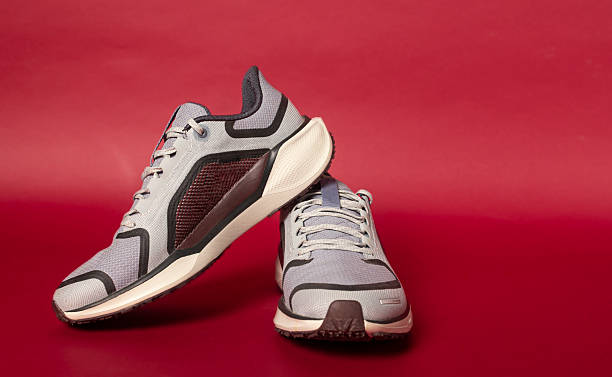 istock Pair of modern grey running shoes leaning on red background 2214239918