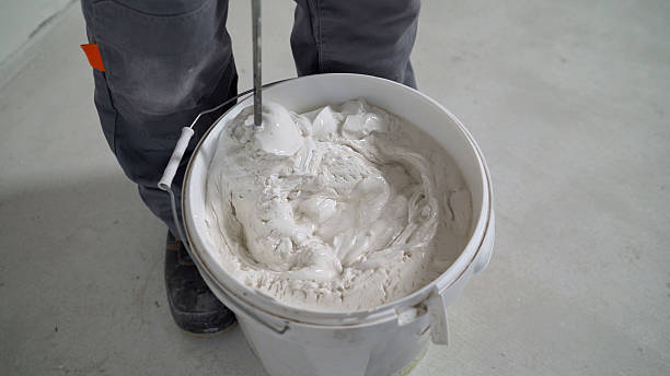 istock Mixing white plaster in a bucket with a stirrer. Close-up. White solution in a bucket, mixed with a mixer. A worker mixes plaster in a bucket to level and putty the walls of an apartment using an electric drill, close-up. 2214240346