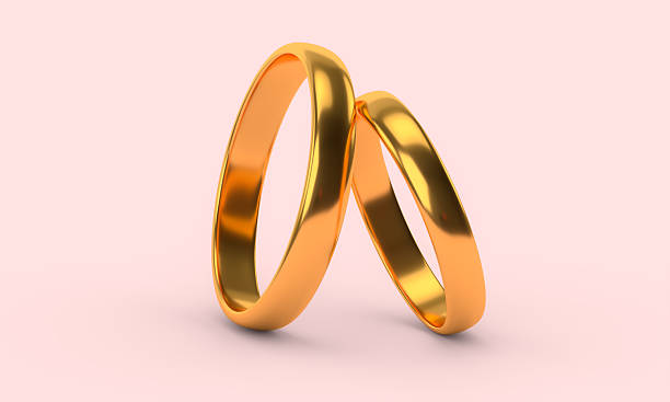 Two shiny golden wedding rings on pastel pink background