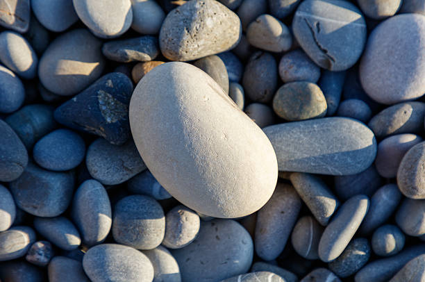 A white rock is sitting on a pile of rocks. The white rock is the only one that is not gray