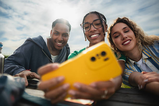 istock Three young adults taking a selfie with a yellow smartphone outdoors 2214245400