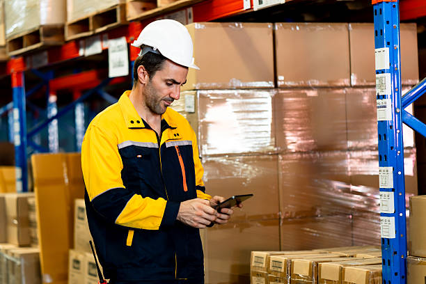 istock Logistics staff in safety uniform using digital tablet checking stock near large cardboard boxes in warehouse, adult Caucasian man with white helmet working supply chain management job environment 2214248723