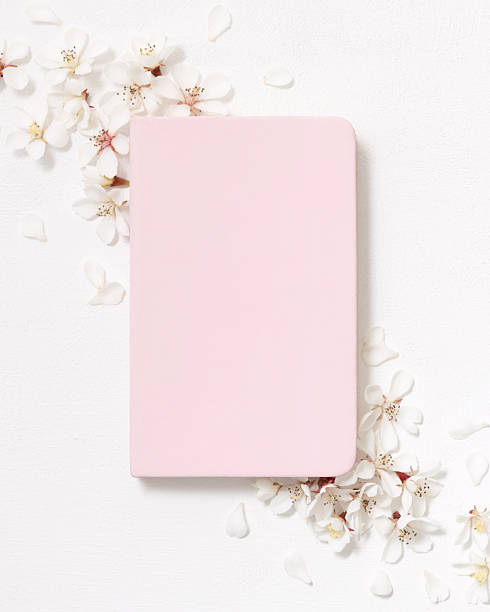 Light pink blank notebook near white cherry flowers top view, spring wedding mockup