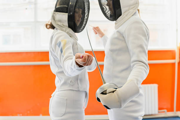 istock Female fencers touching tips before match in bright hall. 2214249189