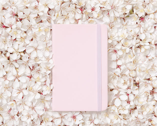 istock Light pink blank notebook over white cherry flowers top view, spring wedding mockup 2214249193
