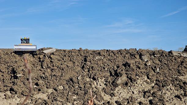 A  yellow Caterpillar bulldozer actively working at a construction or excavation site. The bulldozer is moving over a muddy terrain, pushing large amounts of earth with its front blade. Its tracks are partially submerged in the soft soil, indicating it's operating in a rough and wet area.