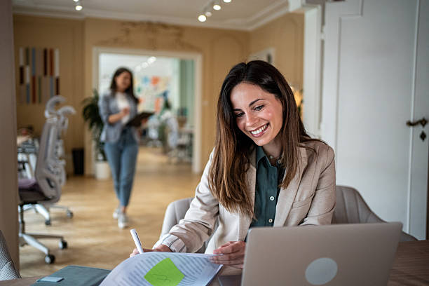 istock Smiling businesswoman working on laptop and taking notes in modern office 2214255460