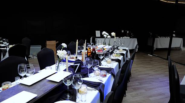 istock Long table beautifully set for a corporate event, featuring white flowers, candles, wine glasses, and elegant black and white decorations in a modern venue with a dark background 2214256592