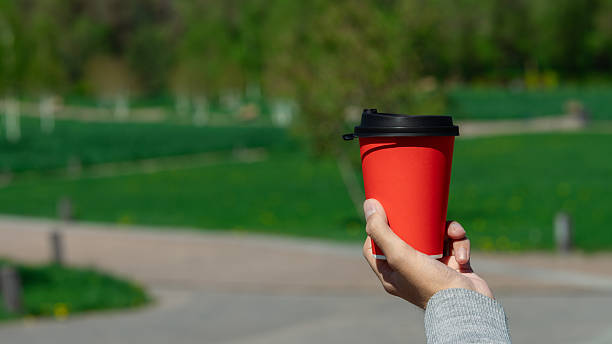 istock Hand holding red coffee cup on park background 2214256717