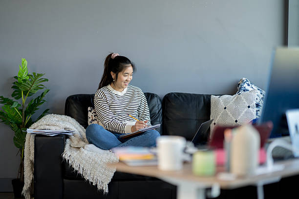 istock Young Woman Sitting on Couch Writing in Notebook at Home 2214257499