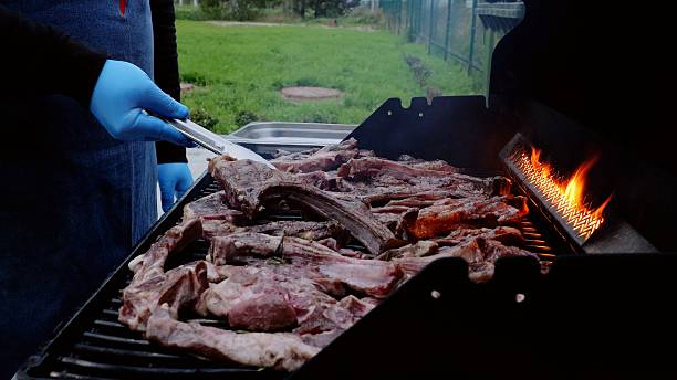 istock Chef wearing blue gloves skillfully grilling lamb ribs on a barbecue, flames dancing from the grill, during an outdoor catering event filled with summer festivities and delicious aromas 2214259720