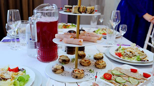 Festive table setting featuring diverse plates with salads, appetizers, cold cuts, stuffed mushrooms, accompanied by red juice pitcher and wine glasses