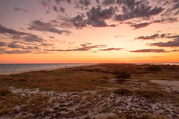 Dramatic sky over a large beach and grassy sand dunes at dusk in autumn. A lonely person by a car is fishing along the shore. Smith point, Fire Island, Long Island, NY, USA.