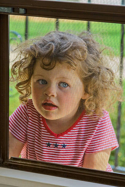 istock Curious cute little girl peeking through screened window. 2214283504