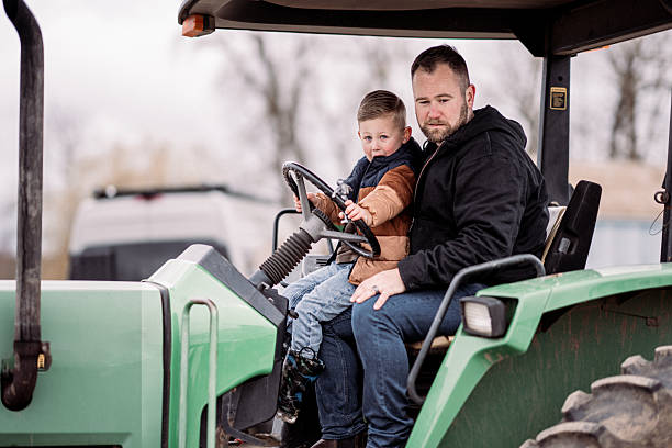Man on the farm driving tractor with his son