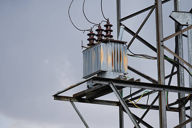 A metal power transformer with visible insulators and rust marks is installed on a steel support tower, set against a cloudy sky. The image reflects the robustness and weather exposure of high-voltage electrical infrastructure in outdoor settings.