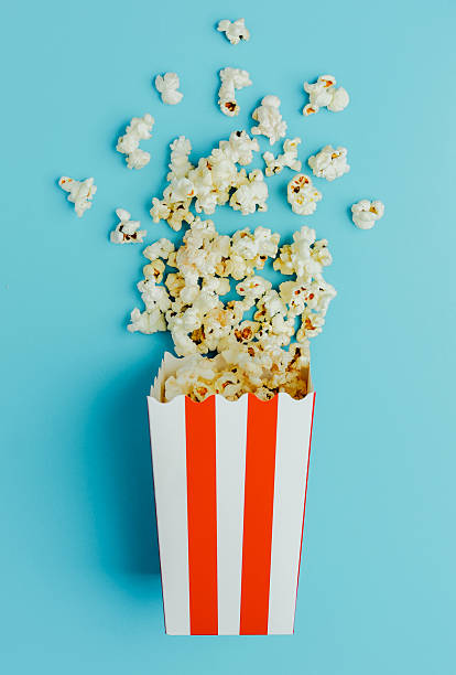 istock Popcorn spills from striped box on blue background in playful setting 2214287693