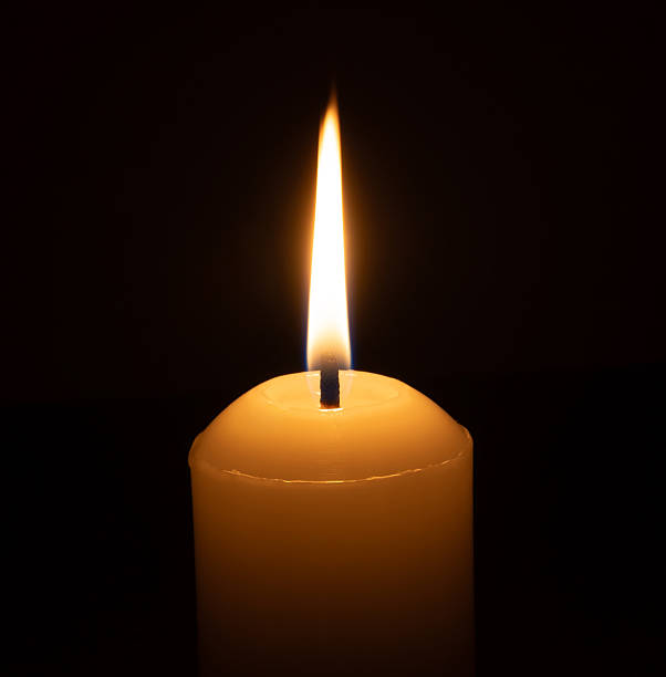 istock A single burning candle flame or light glowing on a big white candle isolated on black or dark background on table in church for Christmas, funeral or memorial service 2214297845