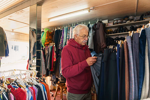 Latin senior man choosing clothes in his small vintage shop, checking the quality of used garment