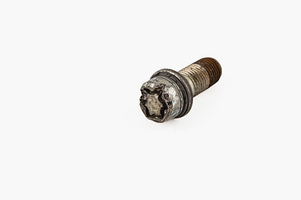 A broken bolt rests on a plain surface, highlighting signs of wear. Nearby, a wheel shows visible damage, suggesting prior use in a mechanical setting.