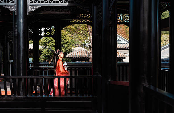 A woman wearing red Hanfu walking gracefully beneath traditional pavilion structure.