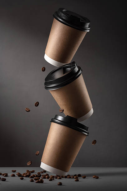Flying disposable coffee cups with roasted beans on dark background