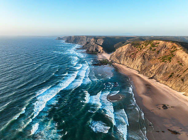 Stunning aerial shot of waves crashing along the rocky coastline at Praia da Cordoama in Portugal