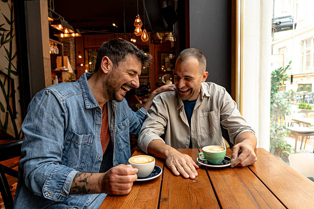 dos hombres alegres riendo y bebiendo café en la cafetería - amigos fotografías e imágenes de stock