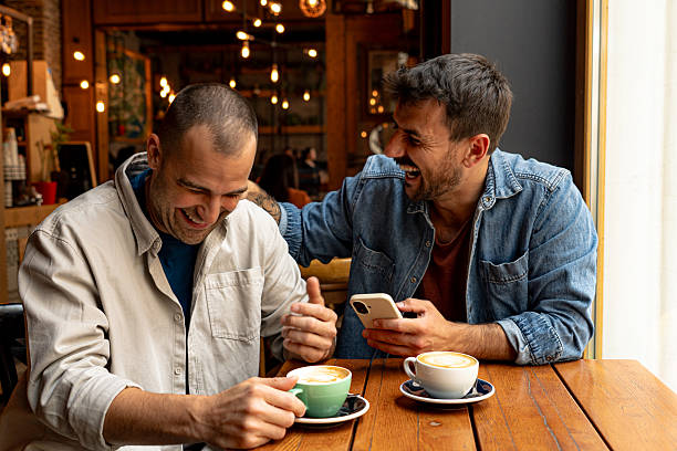 istock Two friends laughing and showing something on smartphone in cafe 2214341044
