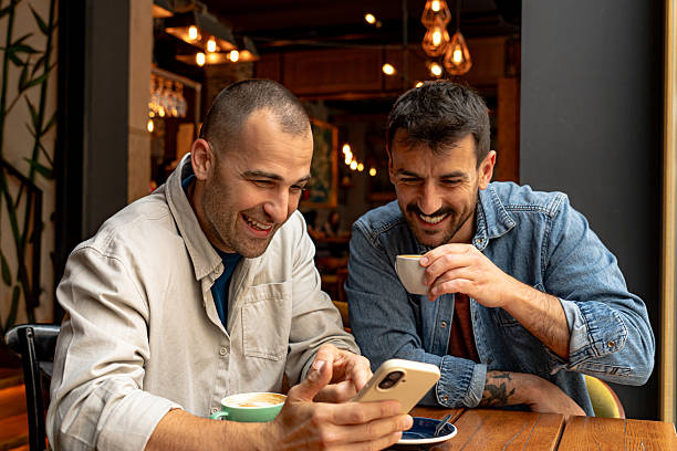 istock Two cheerful men laughing and using smartphone in cafe 2214341046