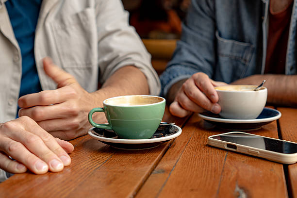 Two friends enjoying cappuccino at cafe with smartphone on table