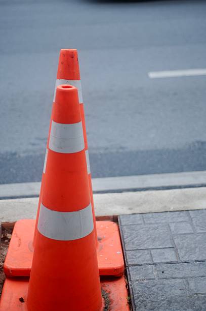 istock Orange traffic cone placed on asphalt with a blurred urban background 2214345892