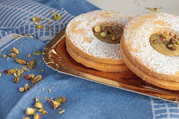 Shortbread dough biscuits with pistachio cream and nuts on gold paper plate. Dessert for party, celebration.