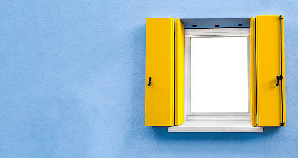 Colorful architectural detail featuring a modern yellow window with shutters set against a vivid blue stucco wall. Captured in a minimalist composition, this image conveys contrast, Mediterranean style, and clean design. Ideal for themes related to travel, architecture, color, and creative backgrounds.