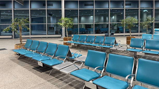 Spacious airport waiting area with empty chairs facing large windows. Empty waiting chairs in the airport building in the evening.