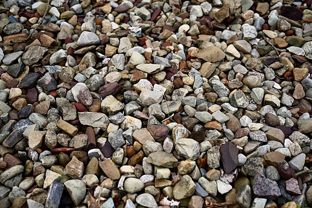 A close-up view of a bed of assorted natural pebbles and small decorative stones in various earthy tones, typically used for landscaping, garden paths, and decorative outdoor spaces.