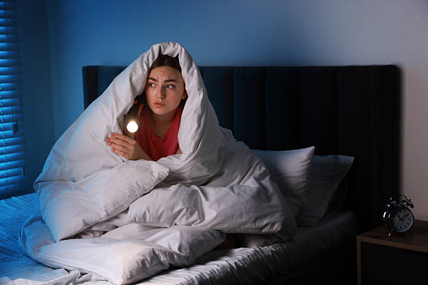 istock Fear of darkness. Scared young with blanket and flashlight on bed indoors at night 2214373018