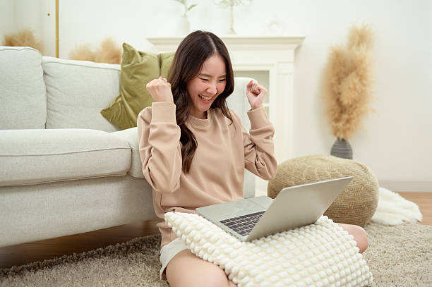 istock Young Asian woman enjoying using laptop computer in living room 2214373859
