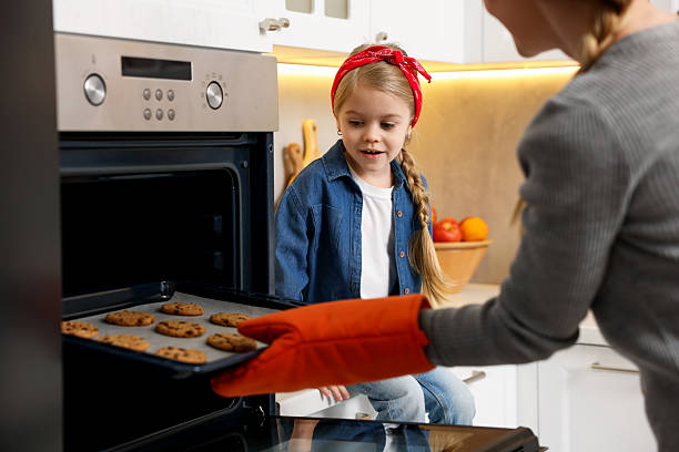 istock Mother and her daughter taking out buns from oven in kitchen, closeup 2214376203
