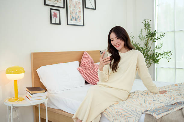 istock Young asian woman using smart phone lying on bed 2214376283
